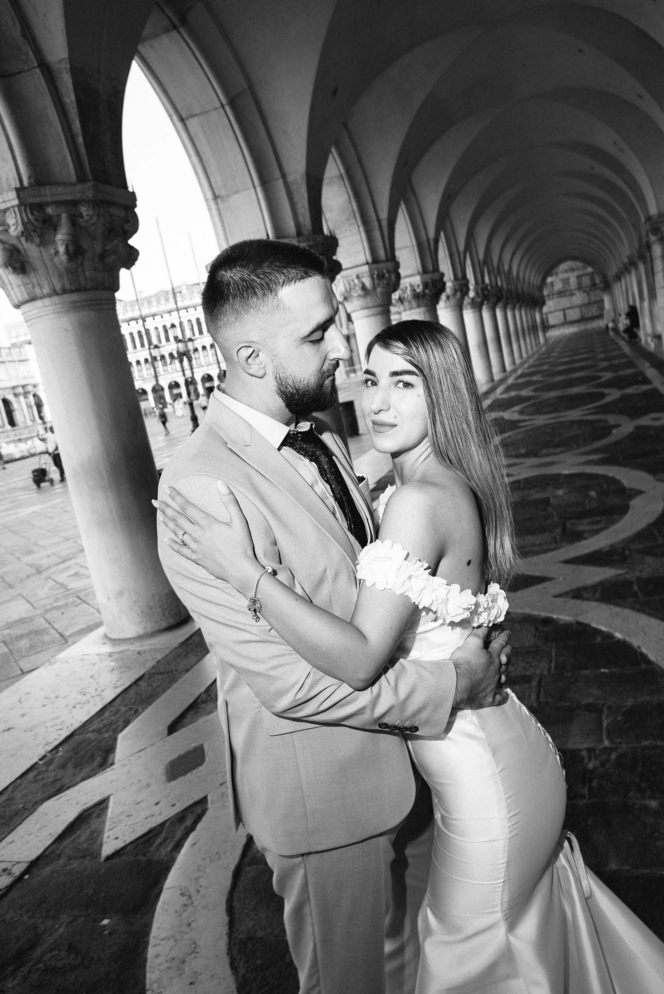 Bride and groom posing in a high-fashion style beneath the Doge’s Palace in Venice, with dramatic architectural details in the background.