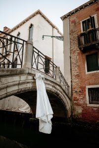 Wedding dress hanging on a small Venetian bridge, surrounded by canals and historic architecture.