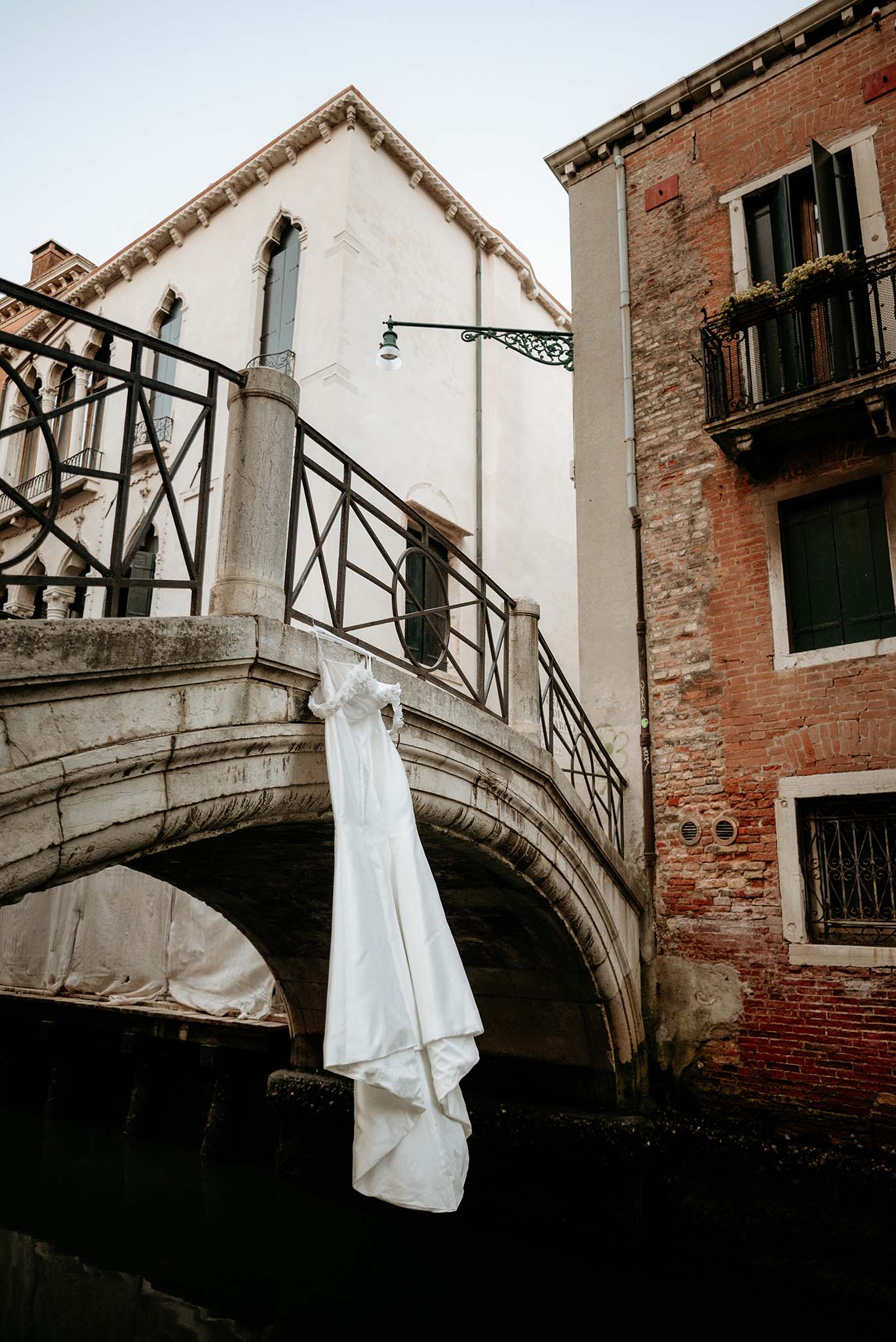 Wedding dress hanging on a small Venetian bridge, surrounded by canals and historic architecture.