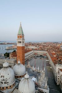 Aerial drone view of St. Mark’s Square in Venice at sunrise, showcasing the basilica, the campanile and surrounding architecture.