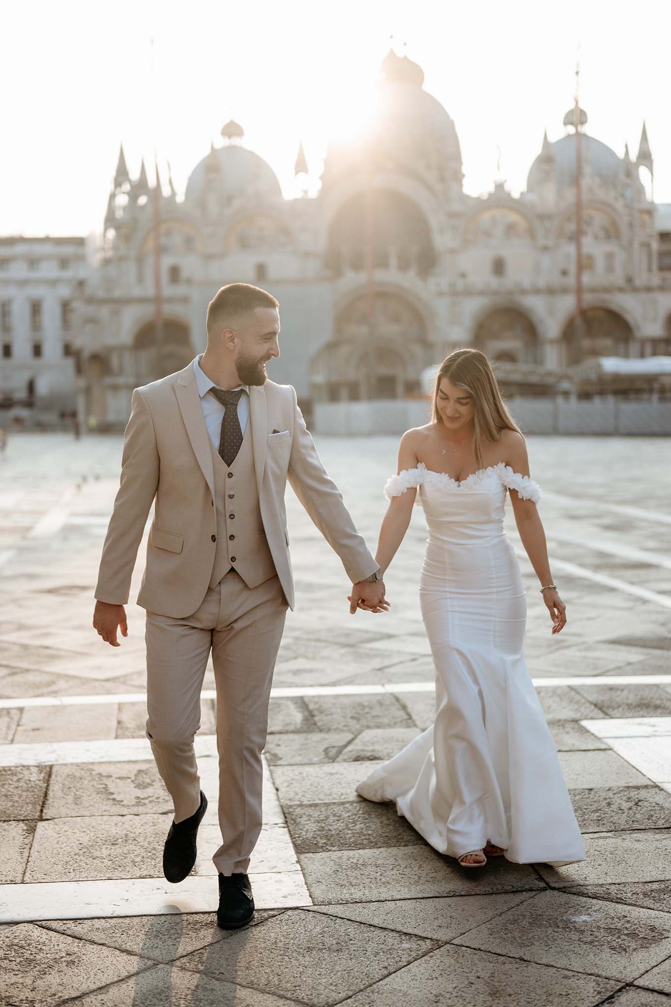 Bride and groom walking at sunrise on St. Mark’s Square in Venice, with warm light illuminating the historic architecture.