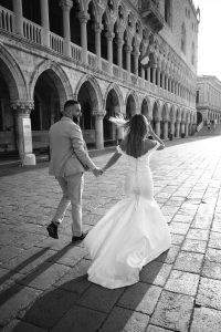 Bride and groom walking at sunrise beside the Doge’s Palace in Venice, with warm light illuminating the historic architecture.