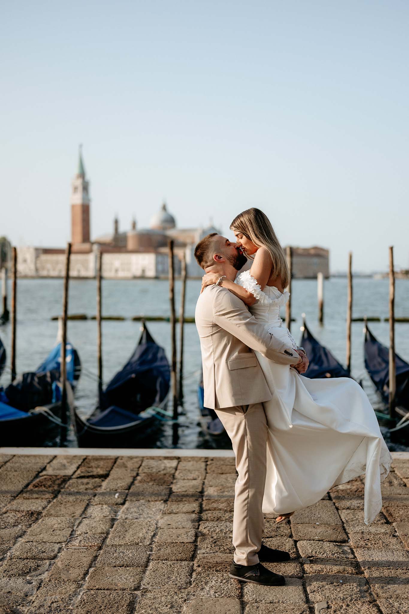 Groom lifting the bride as they kiss in Venice, with San Giorgio Maggiore island in the background.